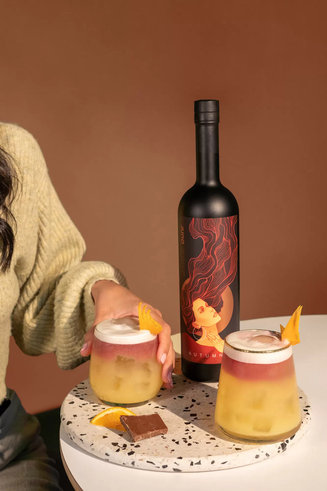 Two Falling Leaves cocktails on a table with a bottle of Juno Autumn 2023 Seasonal Gin
