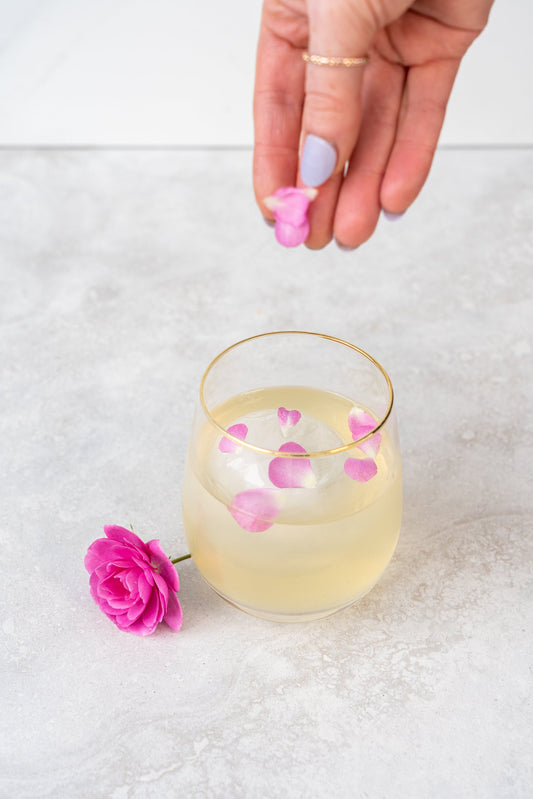 A Yellow Negroni cocktail in a gold-rimmed glass with rose petal garnish