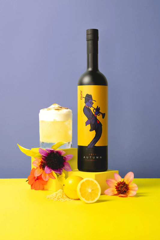 A meringue-topped Cloud Nine cocktail next to a bottle of Juno Autumn 2025 Seasonal Gin and flowers 