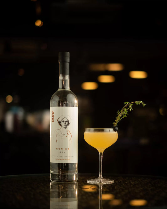 A bottle of Monica's gin next to a yellow cocktail in a moody cocktail bar setting