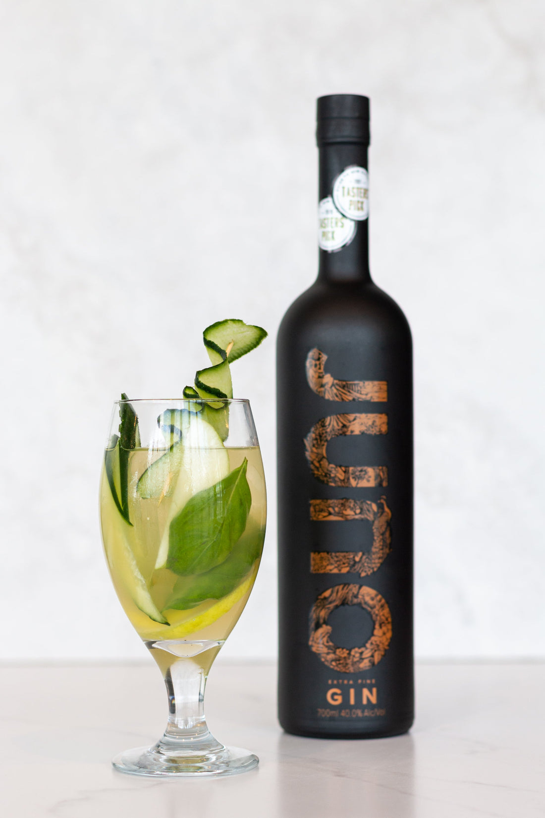 An On the Green cocktail with cucumber garnish next to a bottle of Juno Extra Fine Gin
