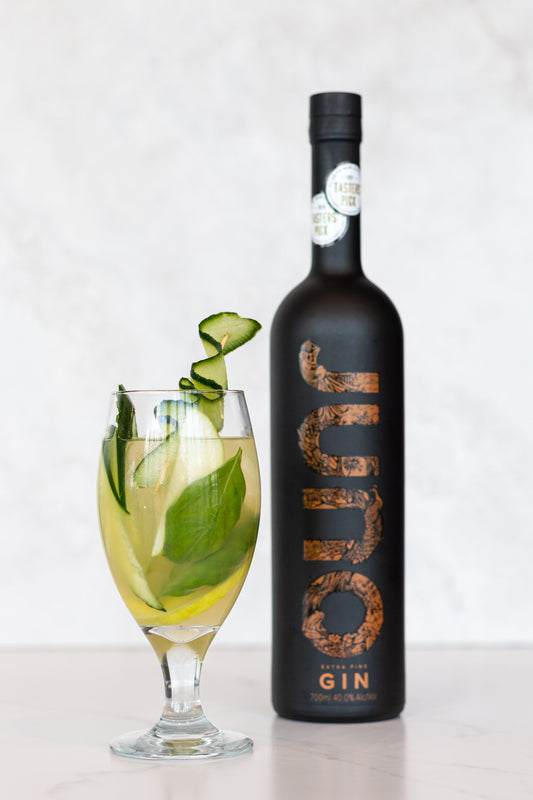 An On the Green cocktail with cucumber garnish next to a bottle of Juno Extra Fine Gin