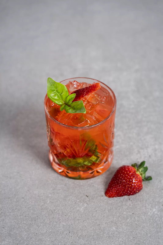 A Strawberry Jubilee cocktail with smashed strawberry and basil garnish