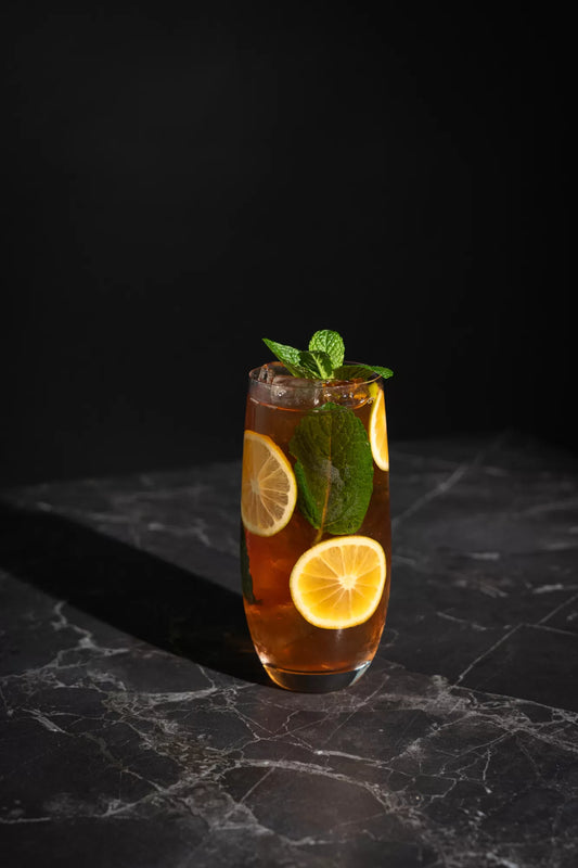 An Iced Tea cocktail in a tall glass with mint and lemon