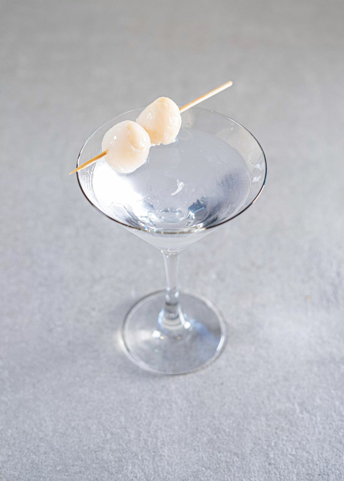 An elegant Lychee Martini in a martini glass with two lychees on a skewer as garnish