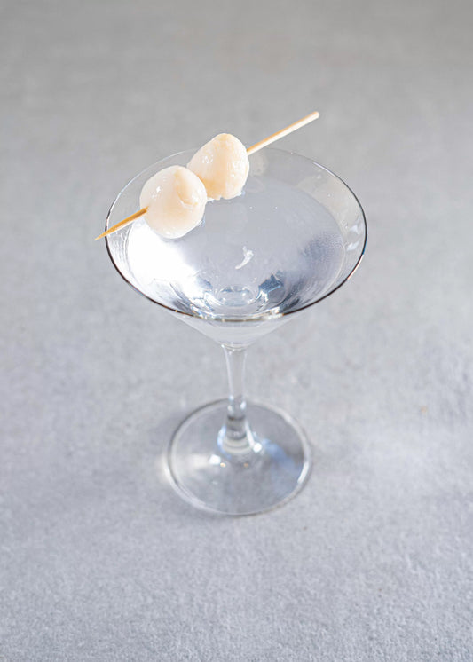 An elegant Lychee Martini in a martini glass with two lychees on a skewer as garnish