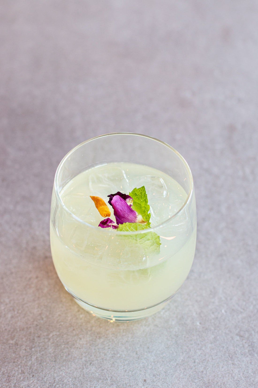 A Summers Kiss Cocktail in a short glass with rose petal and mint garnish